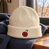 Ecru Little Pit beanie on a blue coat beside an autumn window