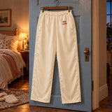 Cream pajama pants with a small hip wordmark on a clip hanger against a blue bedroom door