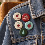 Five colored Pit buttons pinned to textured blue denim